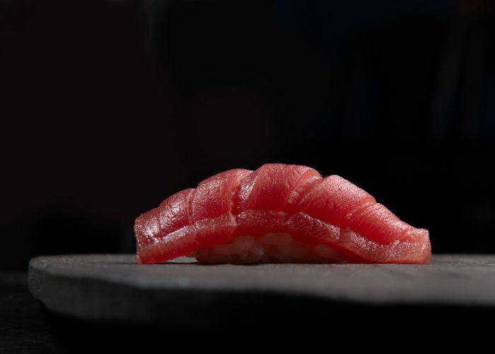 A premium slice of tuna laid over rice, set against a black background.