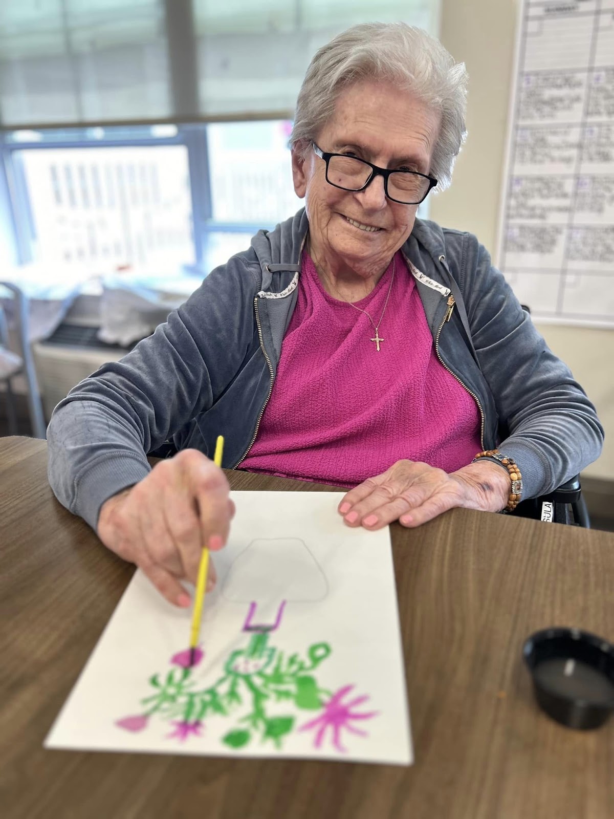 A senior smiling with a drawing on a table in front of her