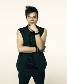 This contain: a picture of  J.Y. Park in a black vest and tie posing with his hands on his chins