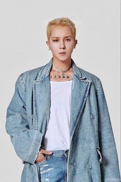 This contains an image of Mino's with blonde hair and piercings standing in front of a white wall wearing a denim jacket