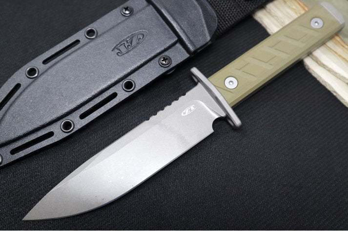 An image showing the ZT 0006 fixed blade on a solid black and wood background. The knife features a clip-point handle and an olive drab handle. Next to the knife is a black Kydex sheath.