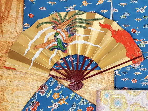 Elegante abanico plegable japonés con diseño de lámina dorada que muestra accesorios de refrigeración tradicionales que realzan la estética de la fotografía con kimono.