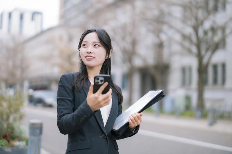 スマホとバインダーを持ち歩く女性