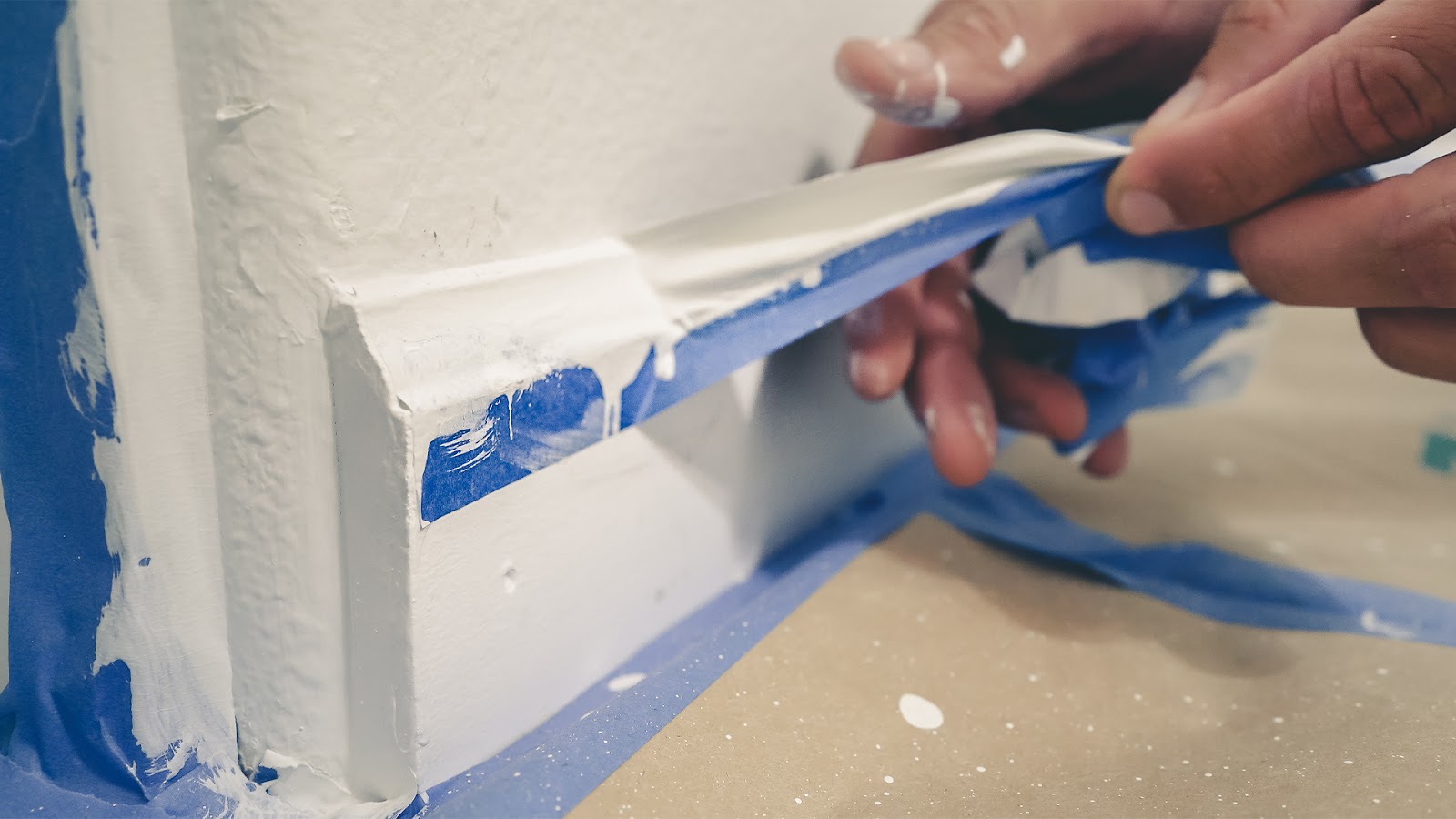 An expert painter's hand is carefully removing blue painter's tape from a recently painted wall to prevent the paint from coming off showing skill and care.