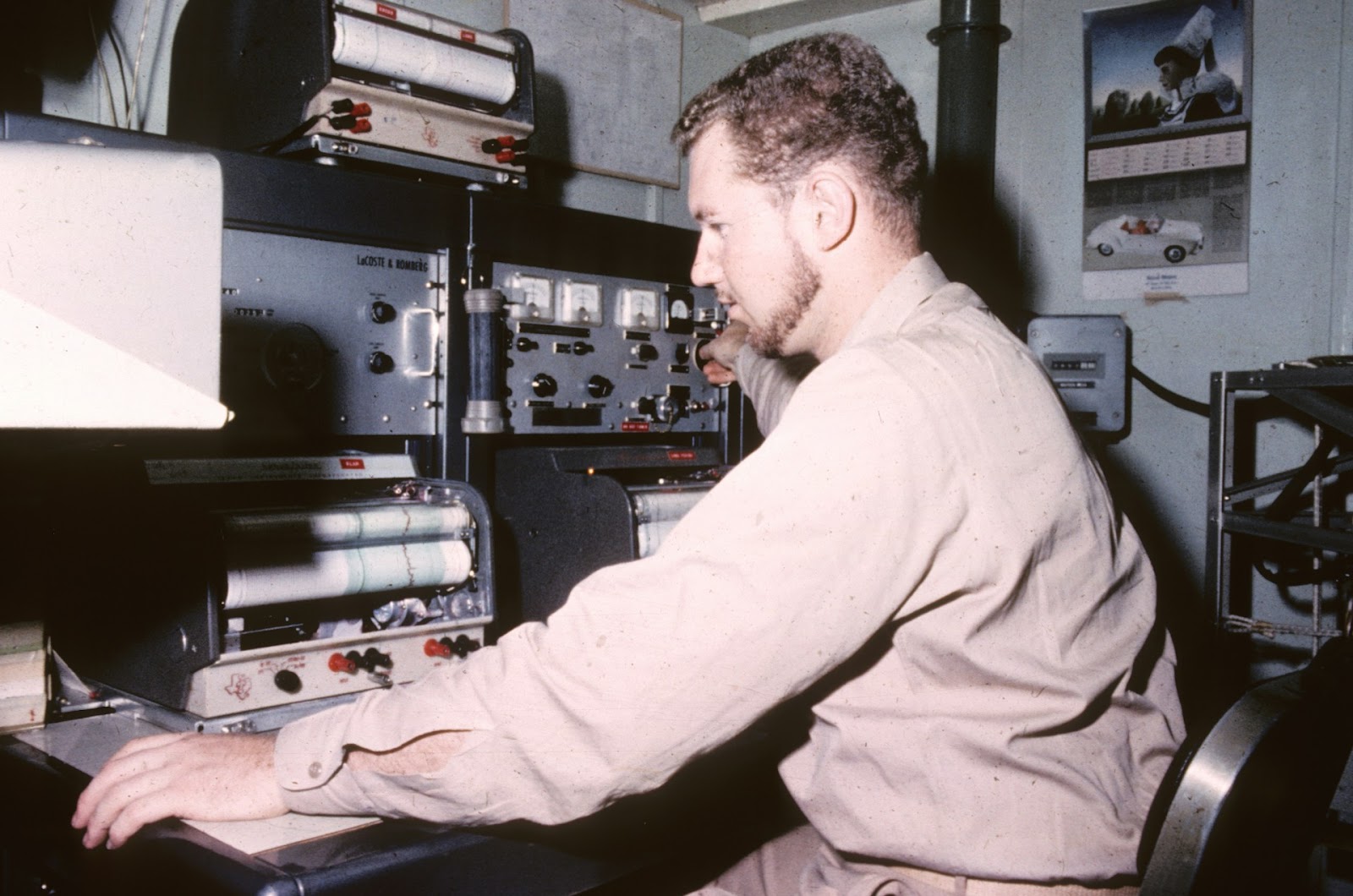 A man seated at a desk, operating various pieces of equipment in a control room.