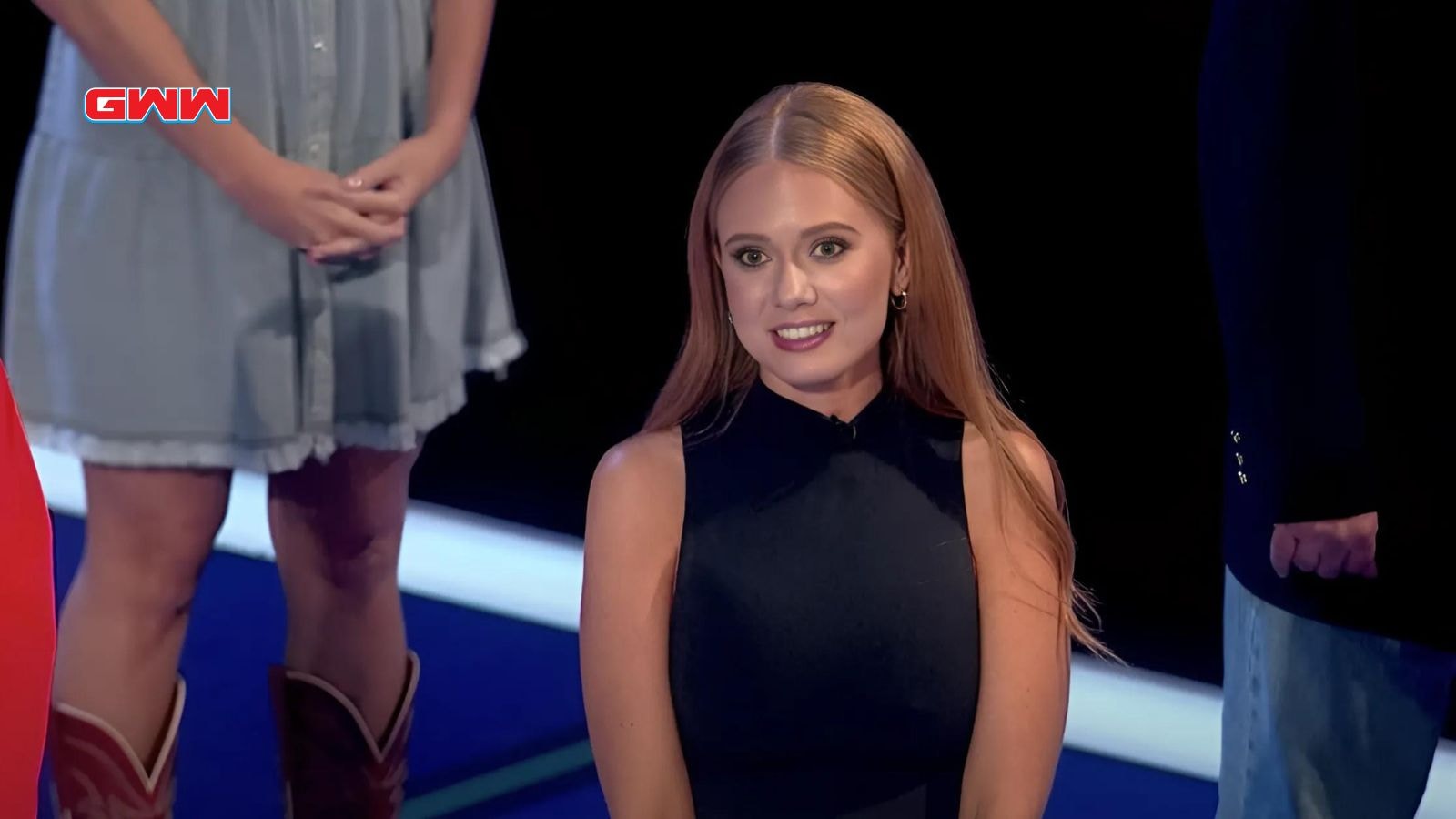 Smiling woman in black dress during a game show appearance.