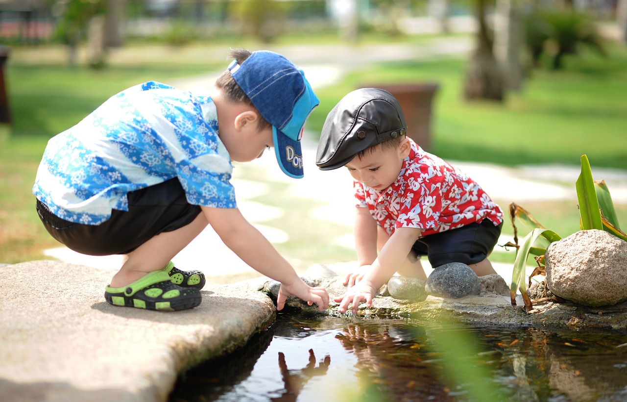 Two young children playing by a pond in a sunny park.