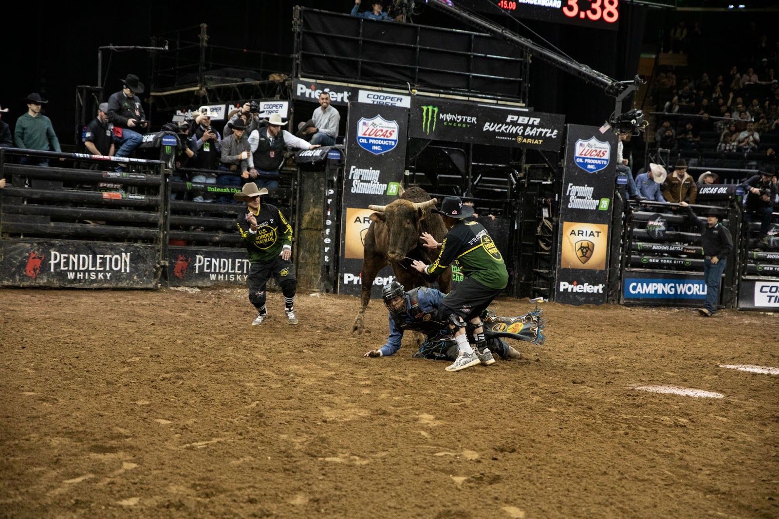 Rider falls to the ground after being thrown from his bull. Referees move toward him to assist.