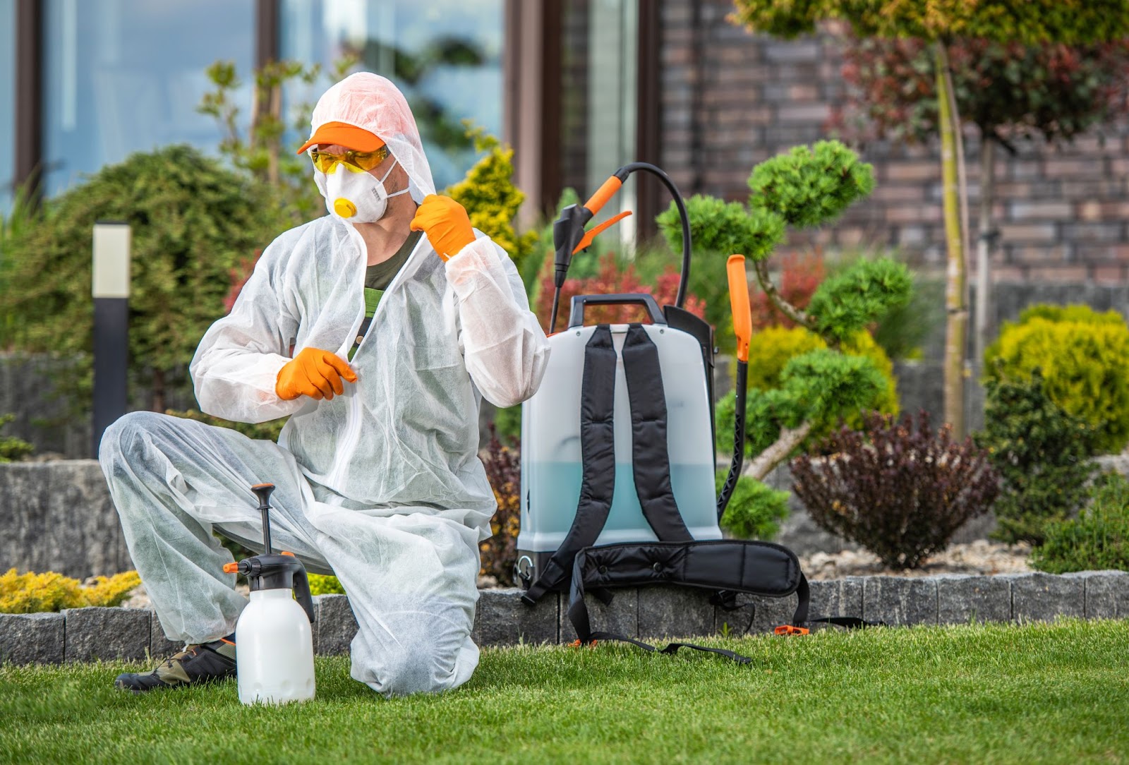 Pest control technician in protective gear preparing to apply treatment in a residential outdoor space.