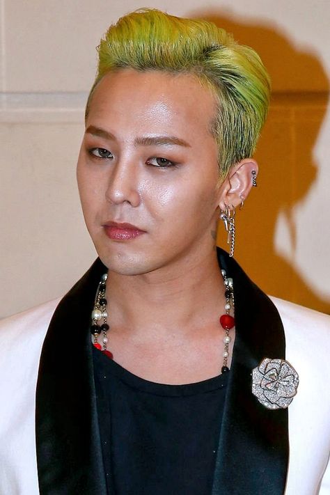 This contain BIGBANG's G-Dragon  with green hair wearing a black shirt and white blazer, standing in front of a wall