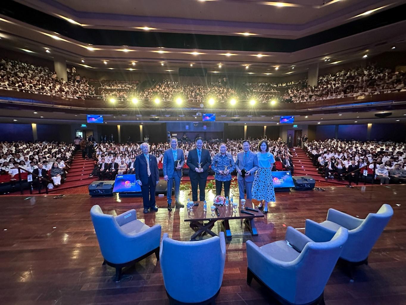 A group of people standing on a stage in a large auditorium

Description automatically generated