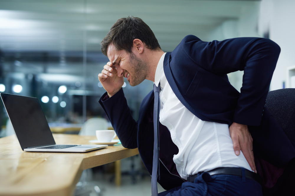 A man seated at a desk, struggling with back pain, illustrating the benefits of lumbar support for better spinal health.