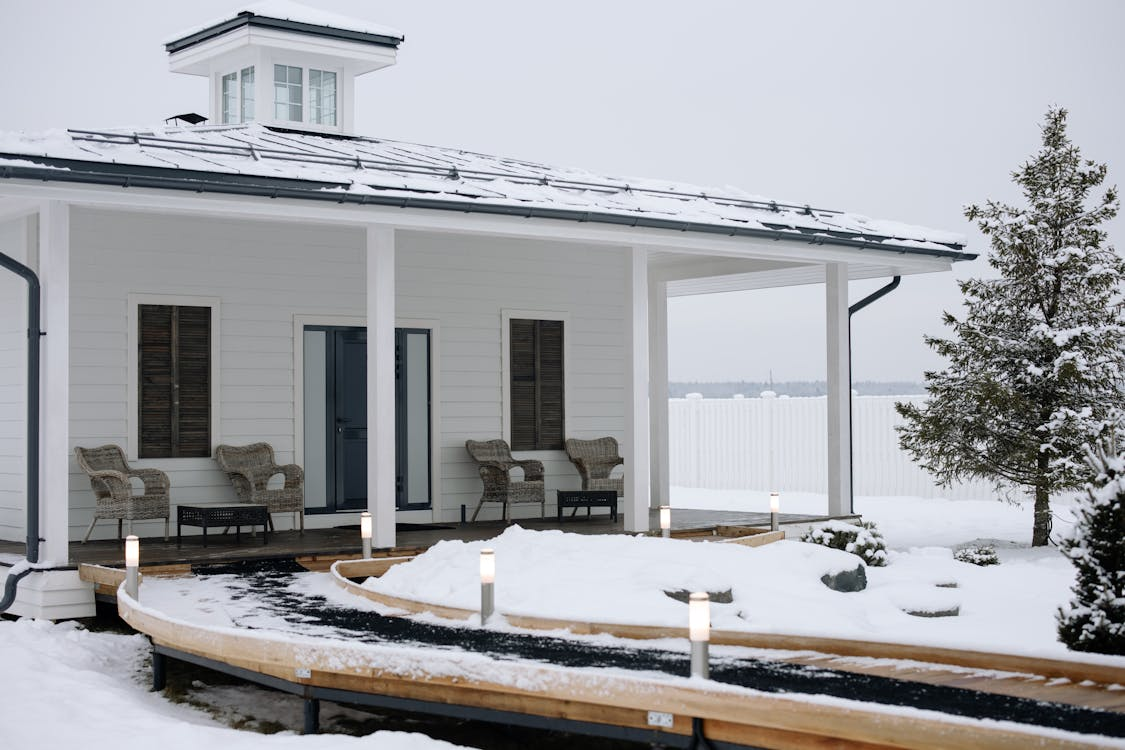 White single-story house with a beautifully lit pathway and snow-covered pine trees.