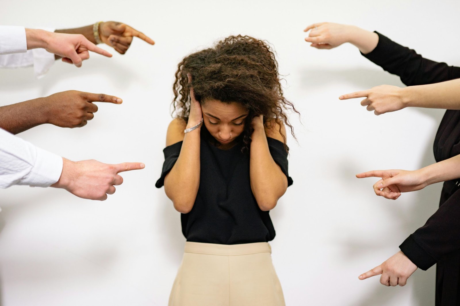 A young lady covering her ears as fingers are pointed at her from all directions