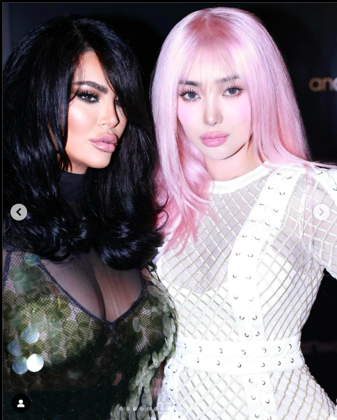 Imagine of Nikita Dragun wearing a white dress and a pink hair abd a lady standing beside wearing a black transparent gown.