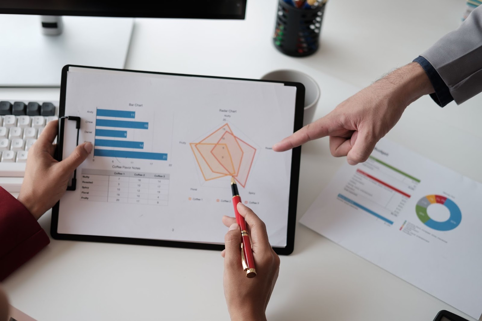 A person holding a clipboard with data and another person pointing at it.