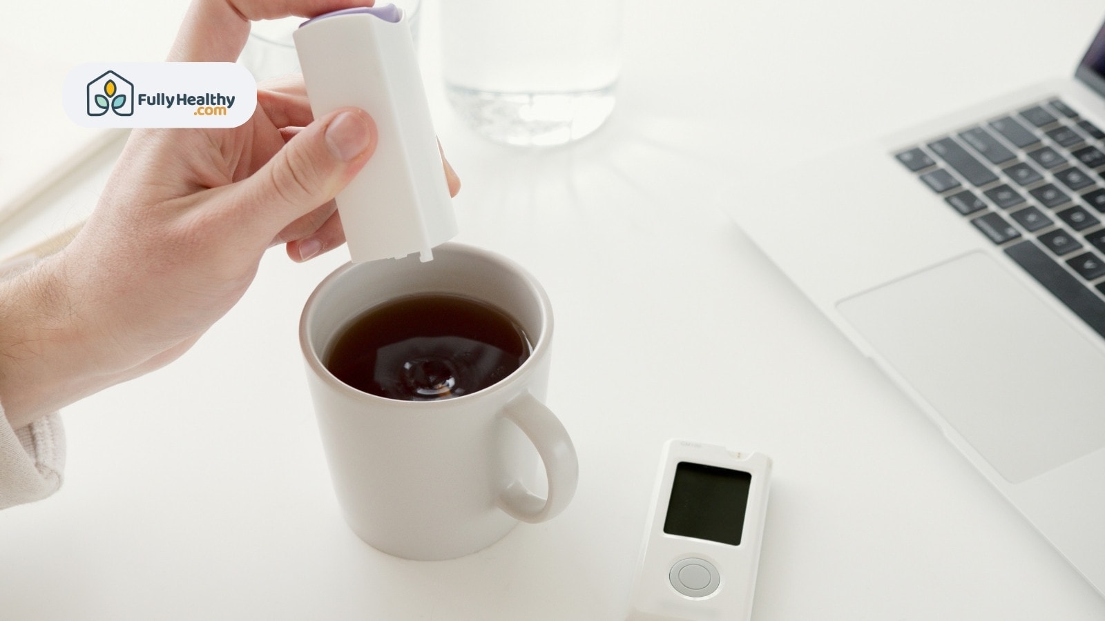 Hand adding sweetener to tea with laptop and glucometer