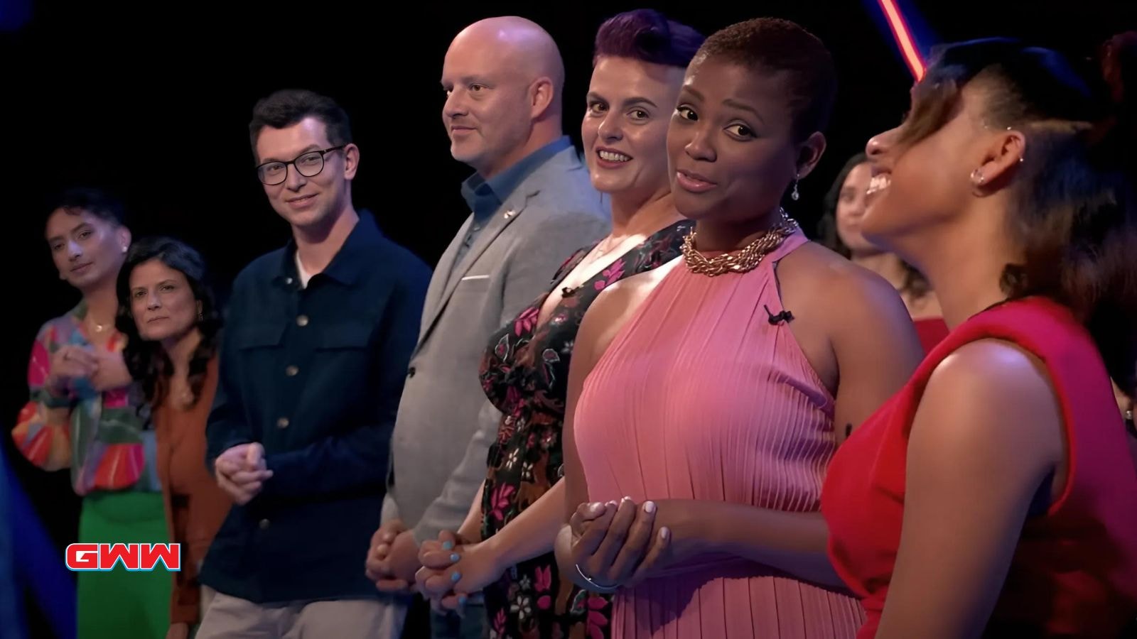 Group of contestants standing together on a brightly lit stage.