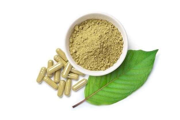 Kratom (Mitragyna speciosa) capsules with powder and green leaf isolated on white surface