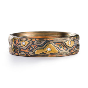 Mokume gane mens wedding ring, flat profile, made with red and yellow gold, palladium and oxidized silver. Patterned to resemble rocky terrain, with tiny diamonds placed organically around the band.