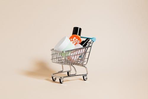 Free Mini shopping cart with cosmetics and a 50% discount sign on a neutral background. Stock Photo