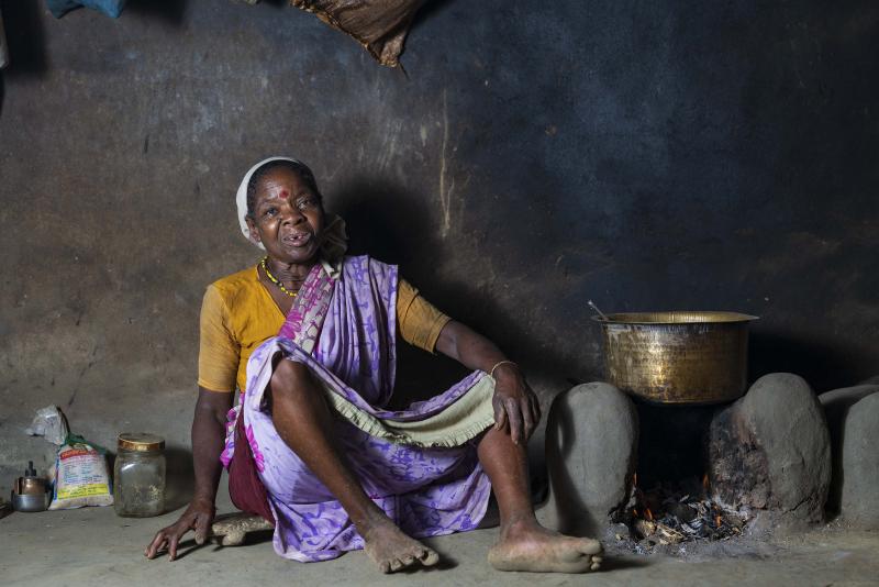 A woman sitting in her rustic kitchen. A towel is wrapped around her head to dry her wet hair.