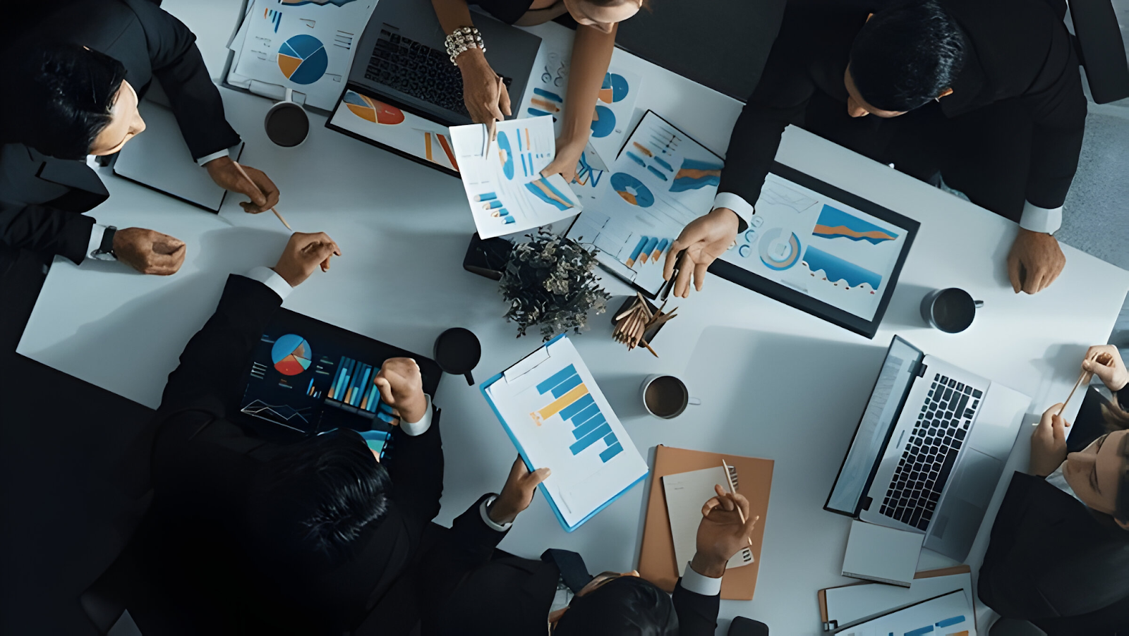 Top view of a business team engaged in strategic financial planning, analyzing charts and graphs on laptops and printed documents to make informed decisions.