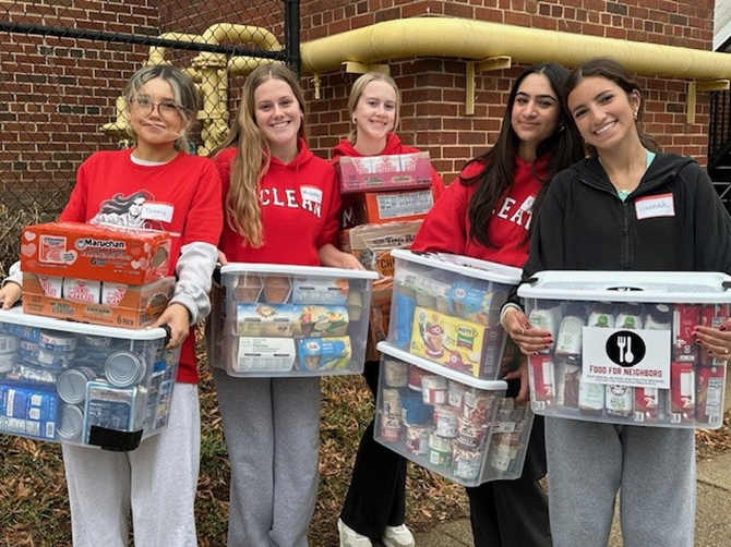 A group of female high school students holding bins of food for donation.
