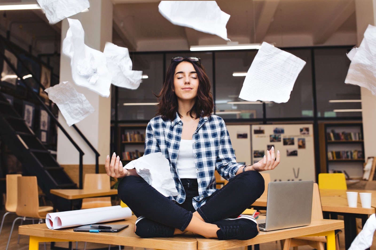 Young pretty joyful woman meditating on table surrounded by work stuff