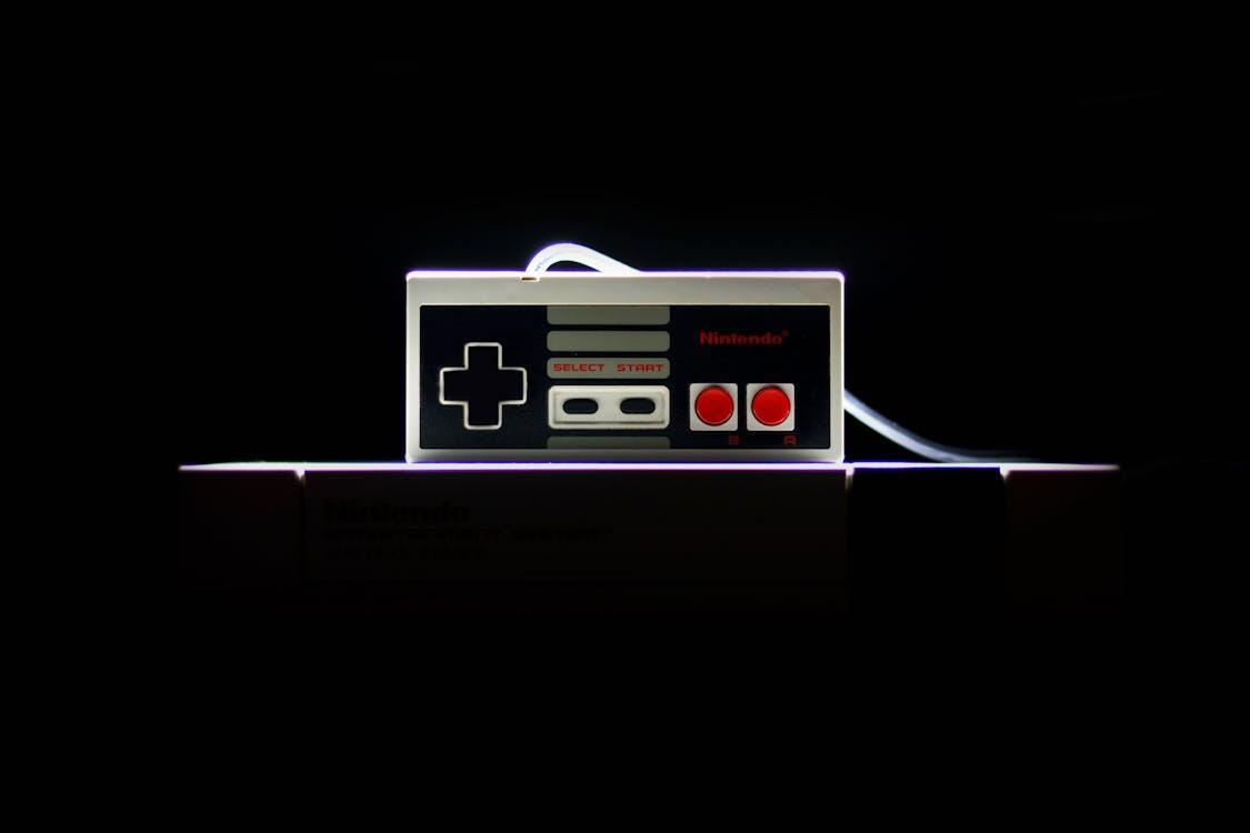 Free A close-up of a classic NES controller with dramatic lighting on a black background, evoking nostalgia. Stock Photo