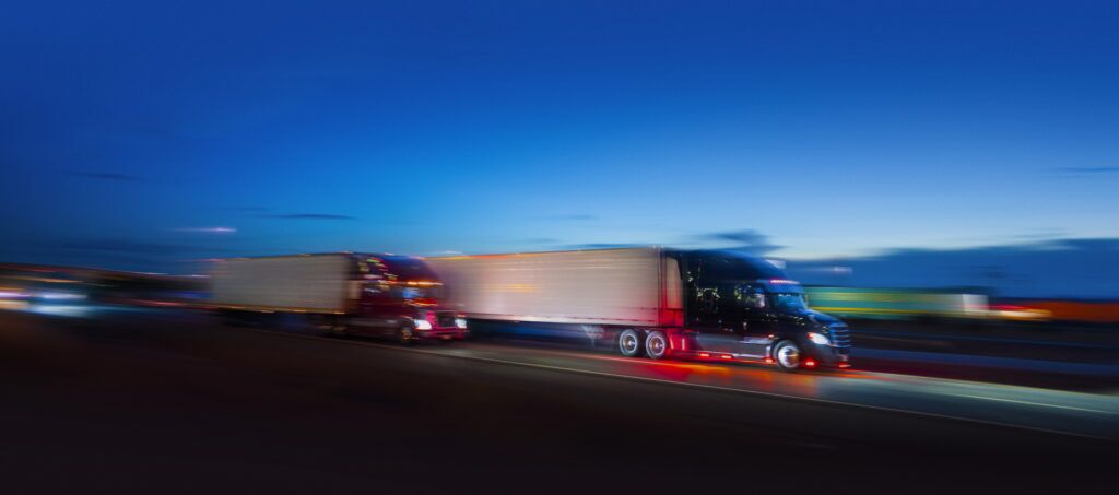 Two semi-trucks driving next to an average passenger car on the highway at night - motion blur 