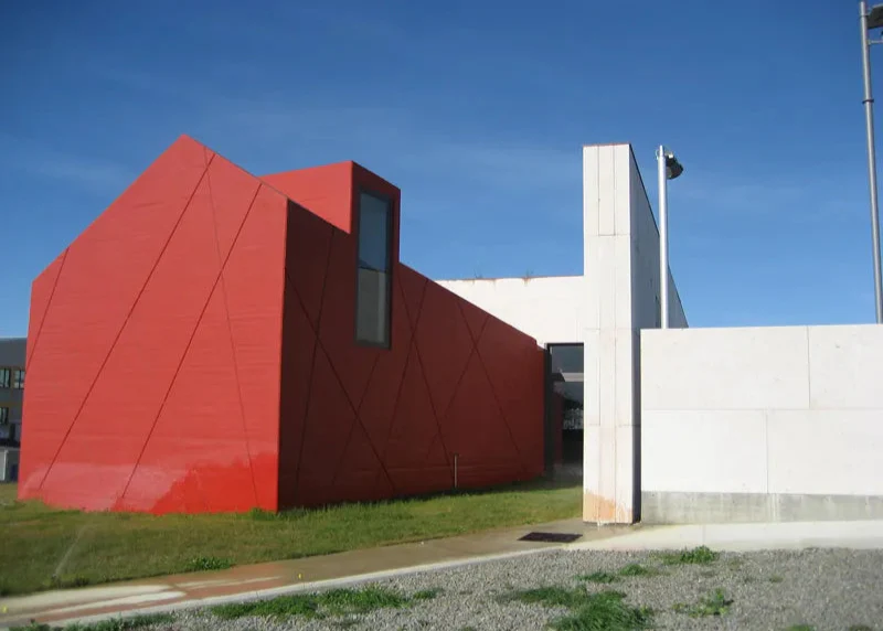 A bright red, shiny, modern commercial building sits on a field of grass.
