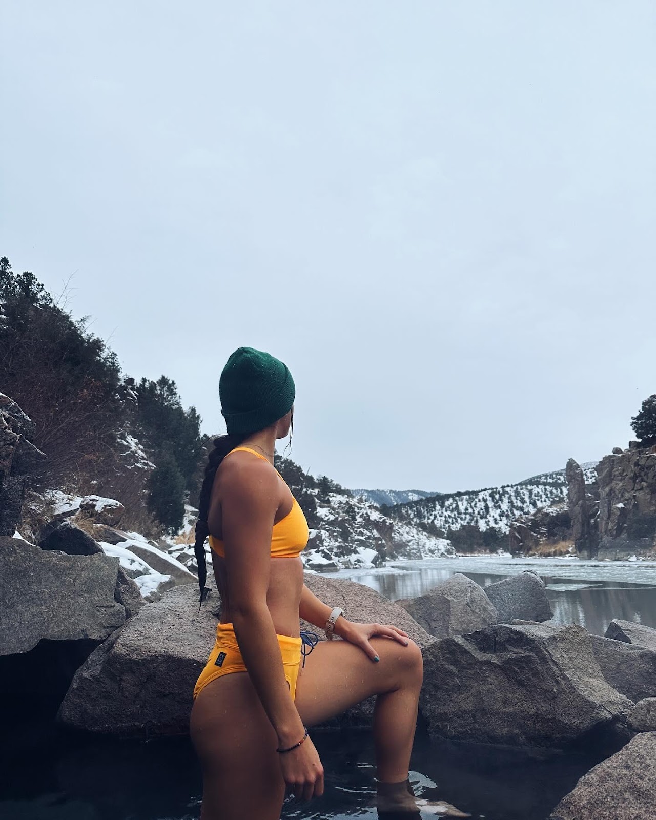 Woman in an orange bikini with a green hat in the lake in front of a snowy landscape