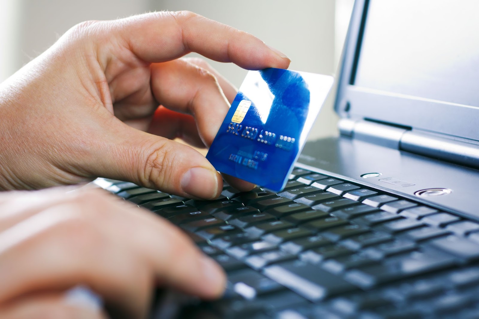 Person holding a blue credit card while typing on a laptop keyboard