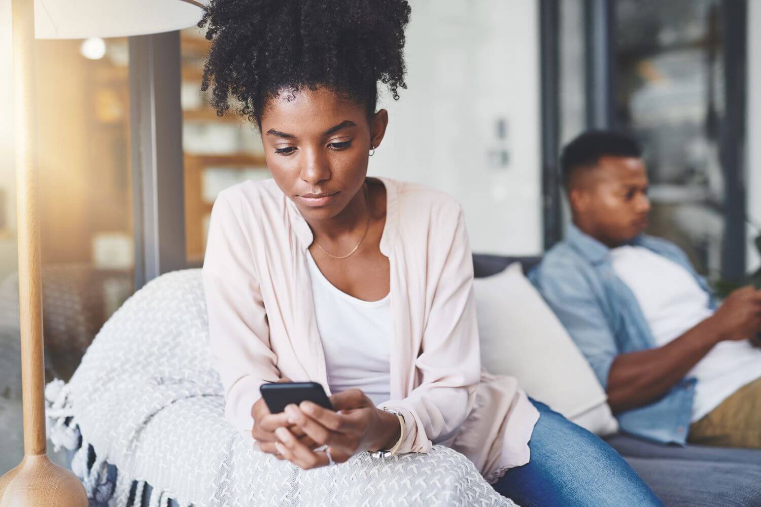 a couple is sitting on opposite sides of a couch, each staring at their cell phones, disconnected