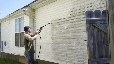 Man using a pressure washer to clean the side of a house.