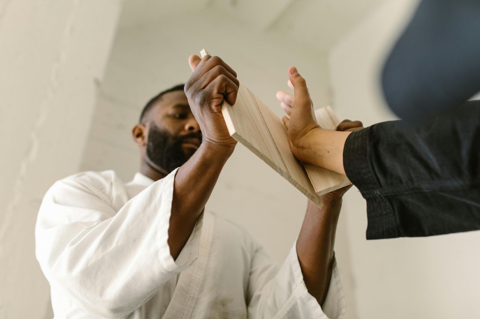 A martial arts instructor holds up a broken board in front of a student who has just punched through it.