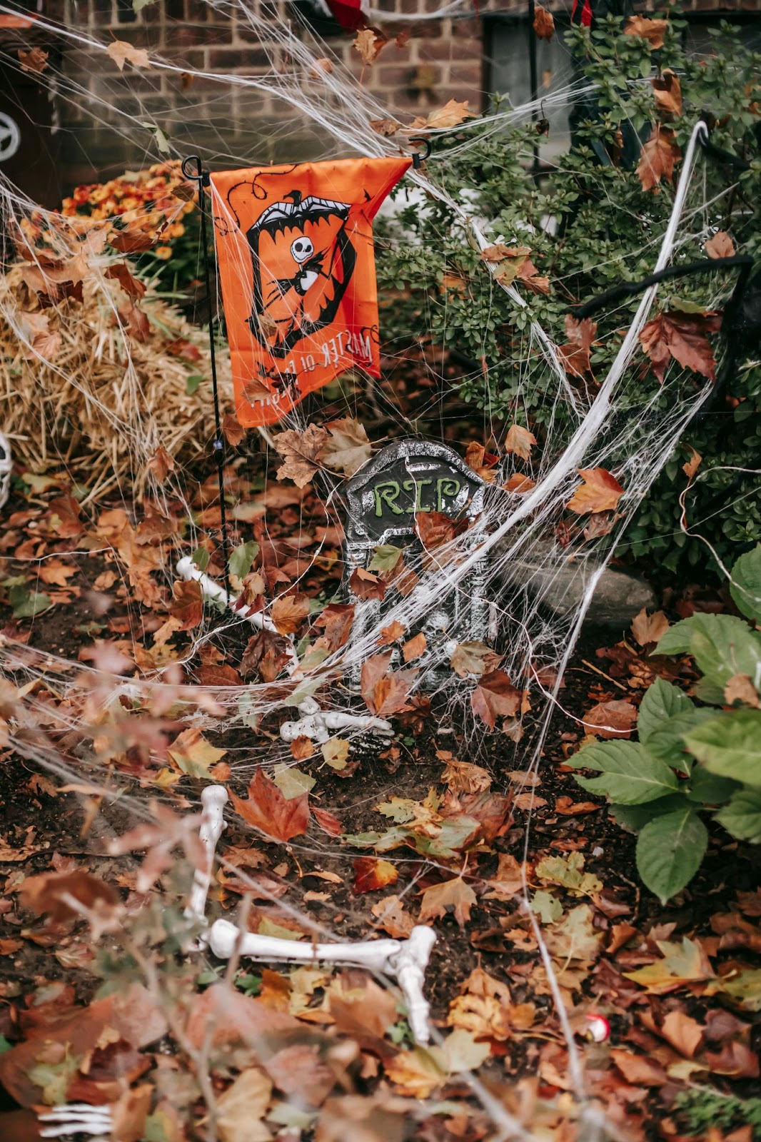 Leaf covered ground with cobwebs, plastic bones, and gravestones. Includes an orange halloween flag