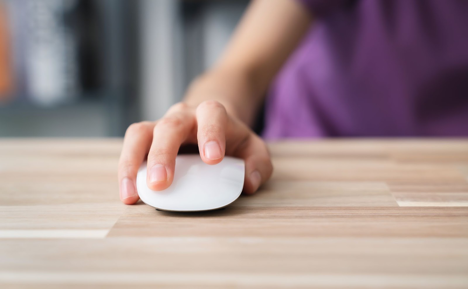 Woman using a mouse on a wooden surface. 