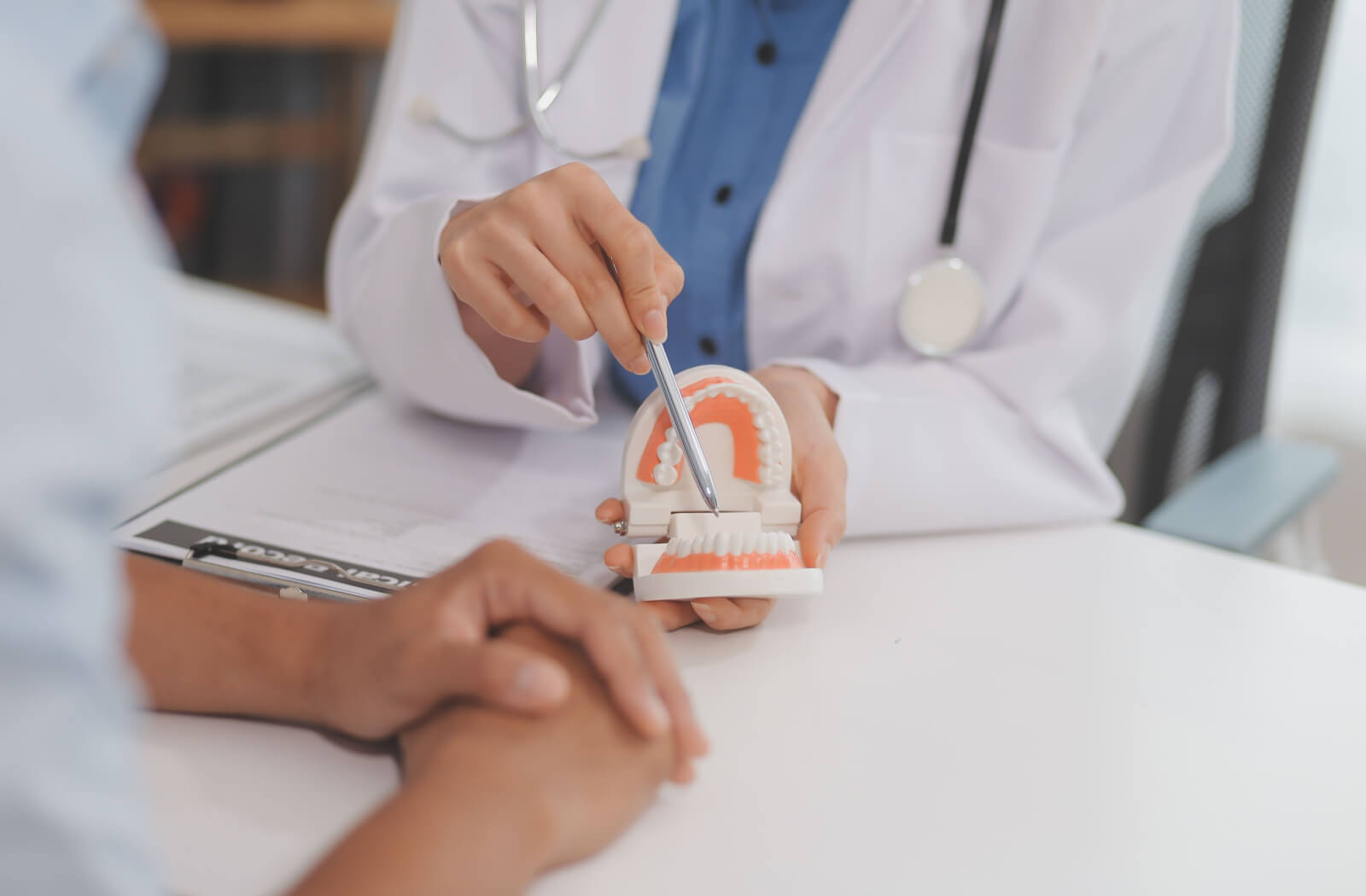 A dentist gesturing with a pen at a model of human teeth, explaining the alternatives to dental bridges.