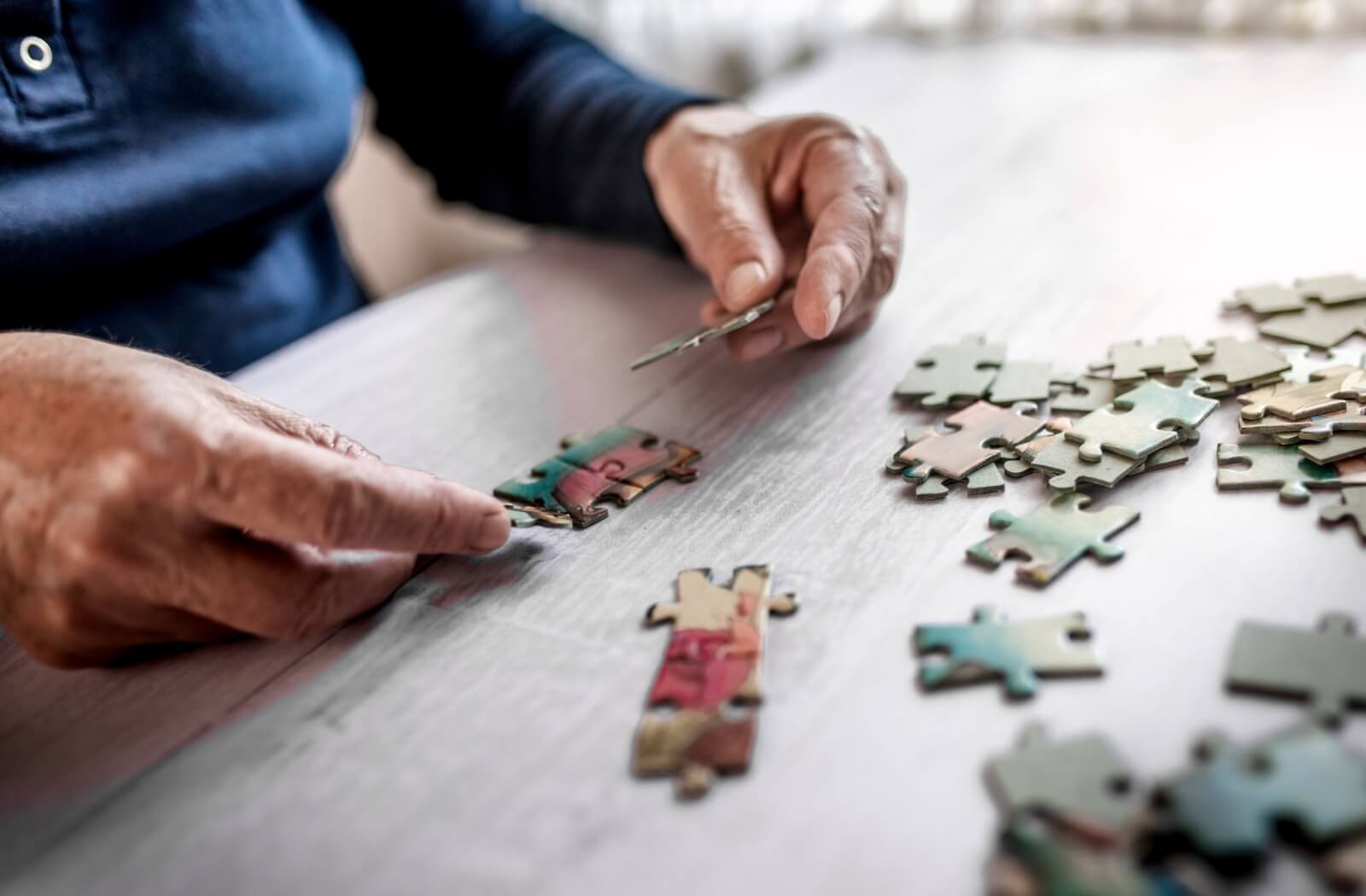 Close-up of an individual holding pieces of a puzzle while building on a wooden table