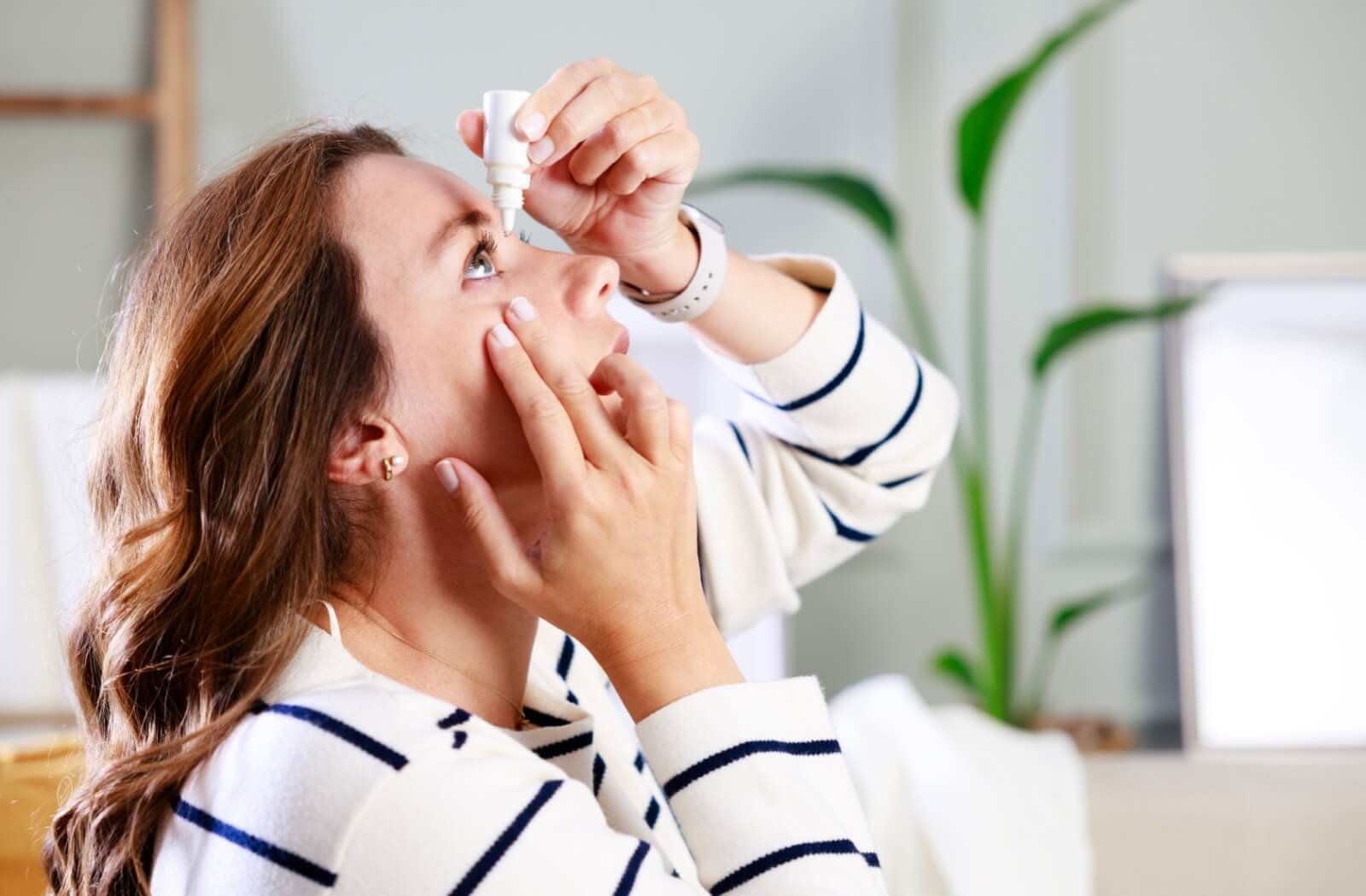 A person pulls down their eyelid to apply medicated drops to treat their eye condition.