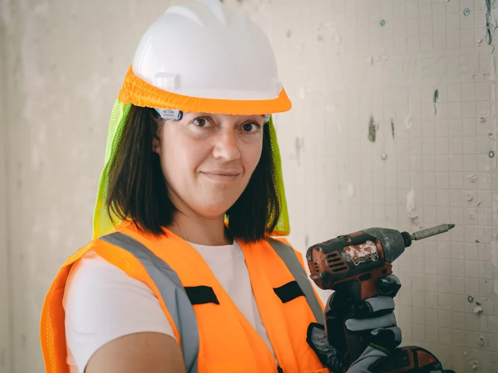 Woman construction worker in safety gear holding drill, highlighting risk management in construction projects
