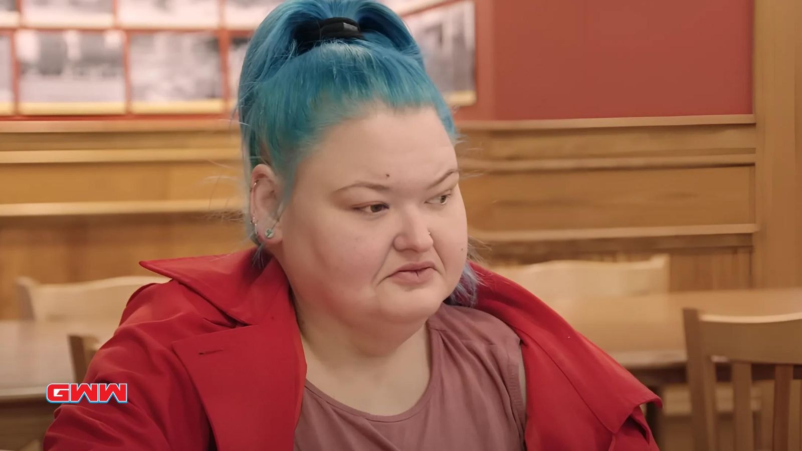 Amy with blue hair in red jacket sitting inside a restaurant.