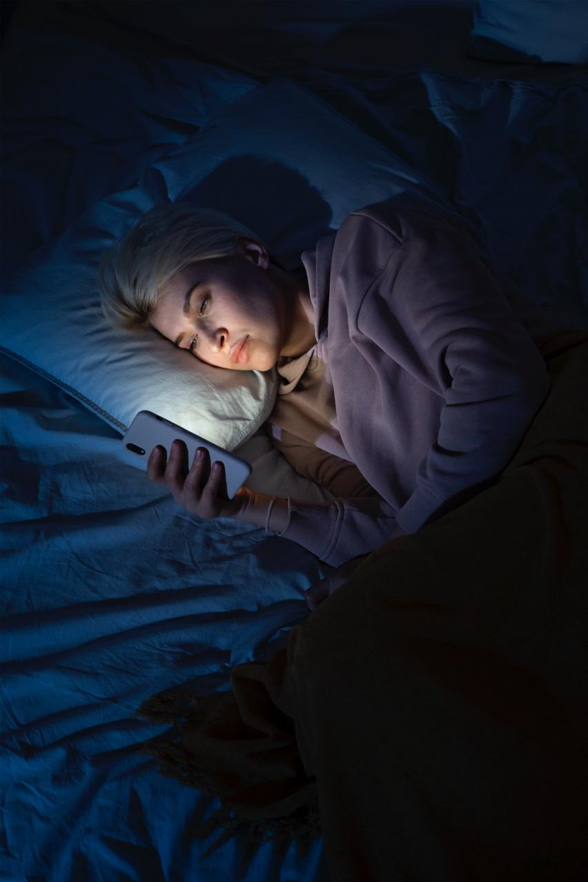 A person lying in bed with a phone

Description automatically generated