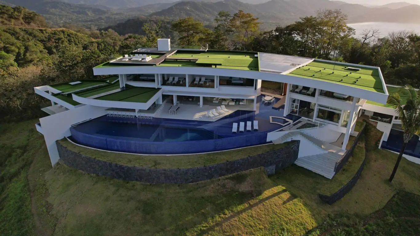 Admire the mesmerizing water and mountain surroundings of this luxury estate. Alt text: A contemporary estate in Guanacaste featuring an expansive infinity pool and a beckoning eco-golf course atop the luxury home amidst a lush natural setting.