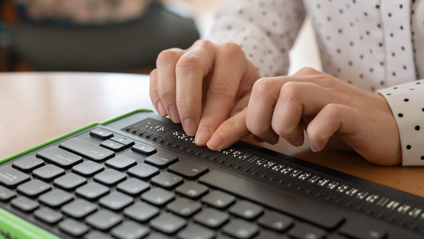 A woman typing on a braille keyboard for a computer with a bright green frame.