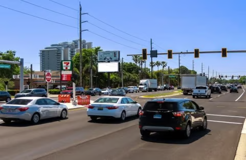 Cars driving on a sunny day with billboards in the background