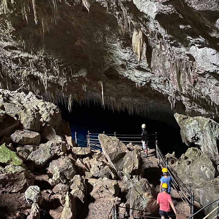 Caverna com estalactites e visitantes explorando através de uma passarela de segurança, ambiente com rochas e formações rochosas.