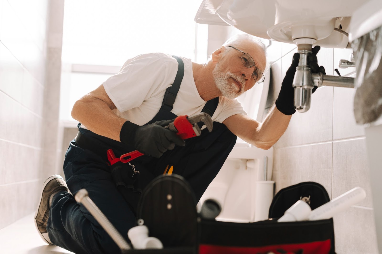 A senior plumber expertly repairs a sink pipe with an adjustable wrench, demonstrating precision and experience in resolving plumbing issues.